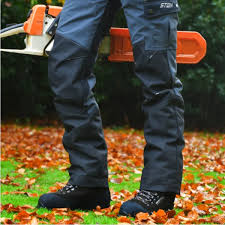 Person wearing dark pants and boots standing on grass with a chainsaw.